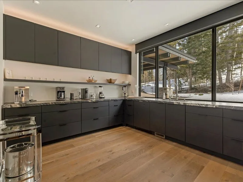 A modern kitchen with dark cabinetry and large windows overlooking trees.