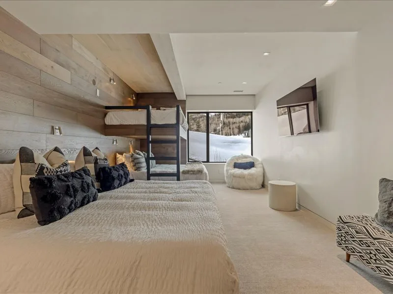 A bedroom with layered bedding and a window overlooking a snowy landscape.