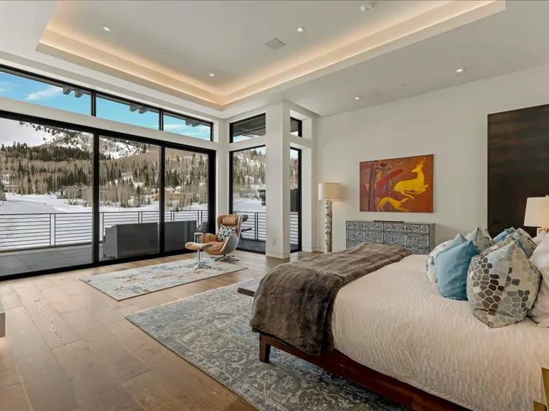 A spacious bedroom with a large bed and floor-to-ceiling windows overlooking a snowy landscape.