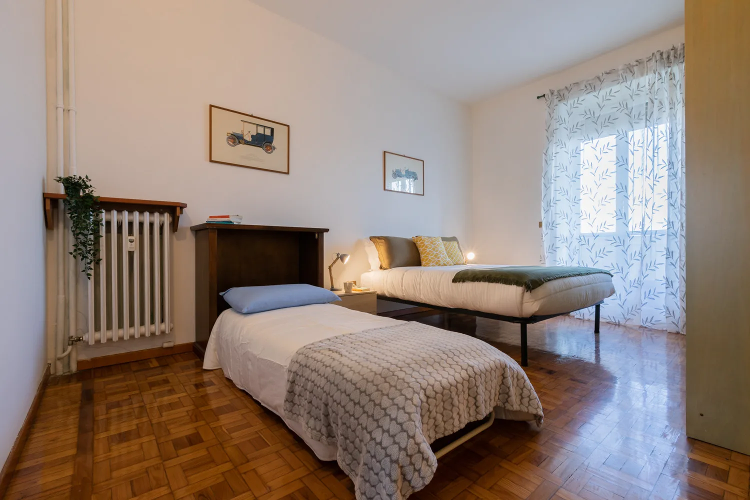 Un dormitorio con dos camas, cuadros enmarcados y una cortina estampada luminosa.