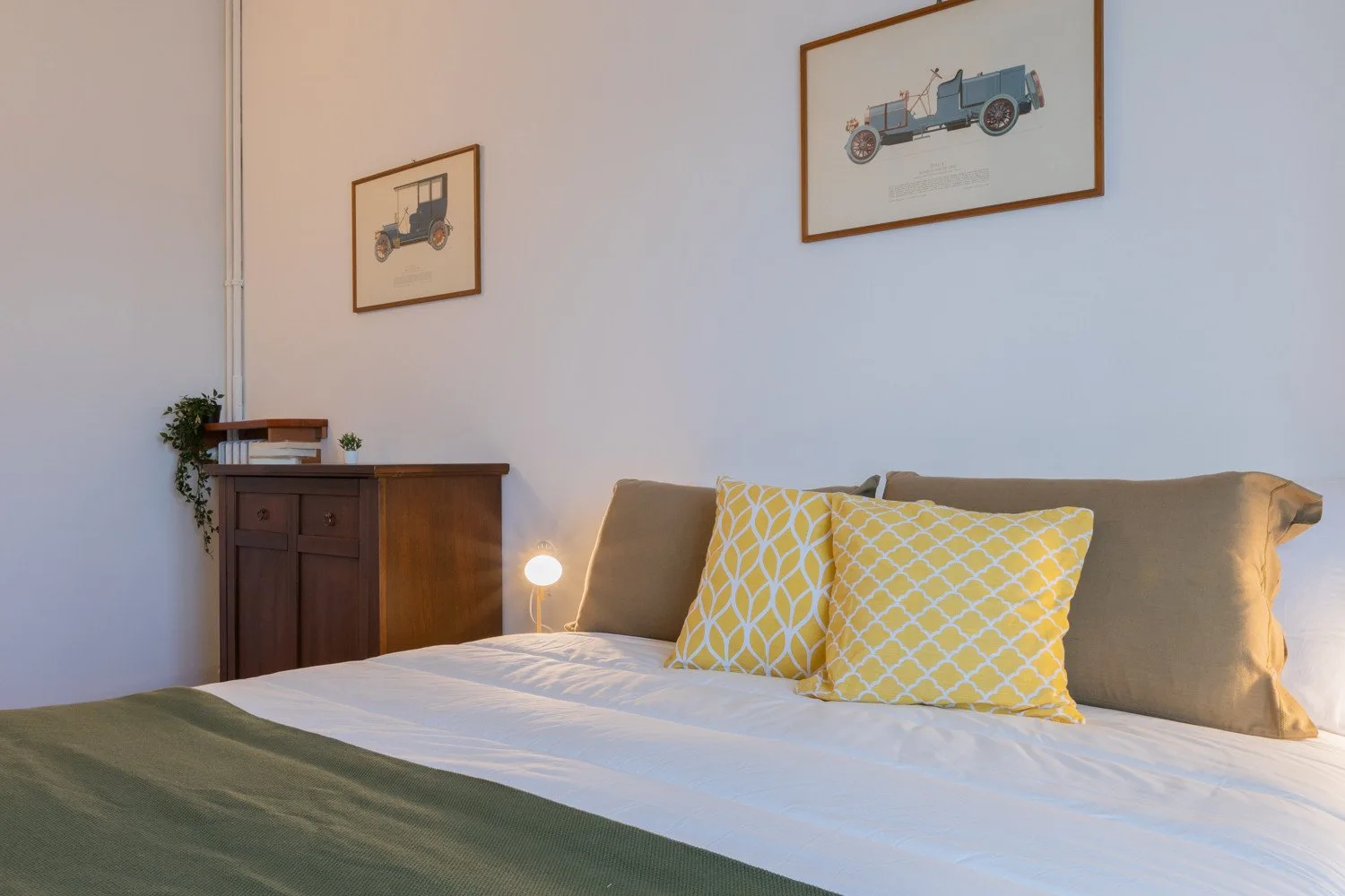 Dormitorio con una cama, cojines amarillos estampados y láminas de vehículos enmarcadas.