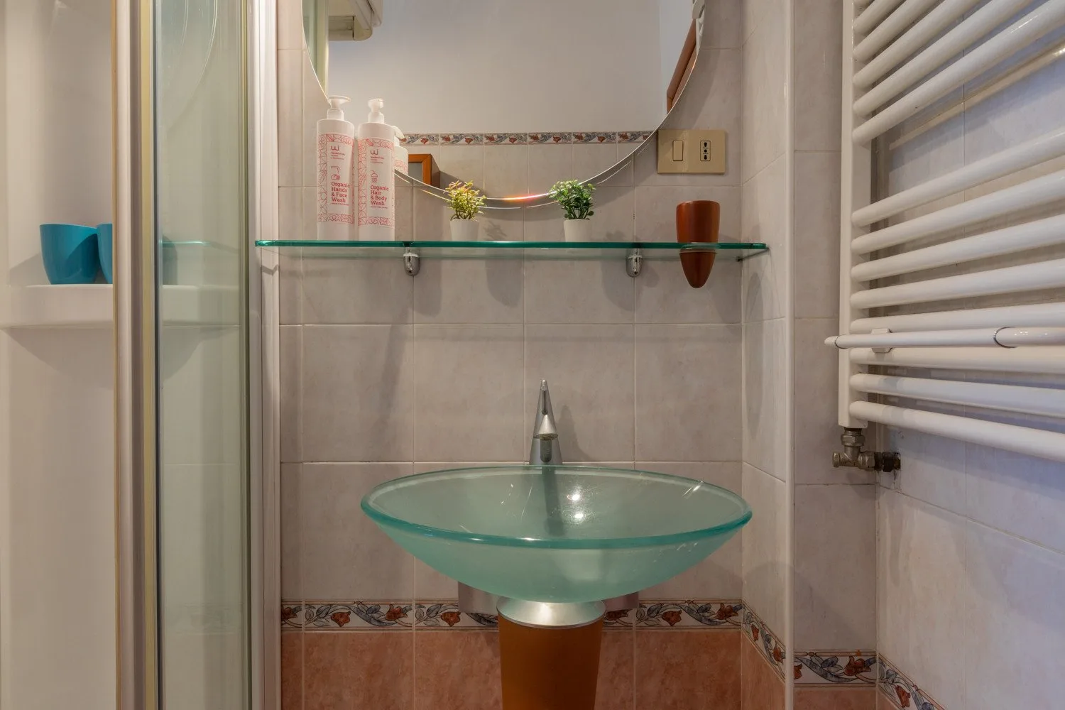 Un baño alicatado con un lavabo de vidrio bajo un espejo.