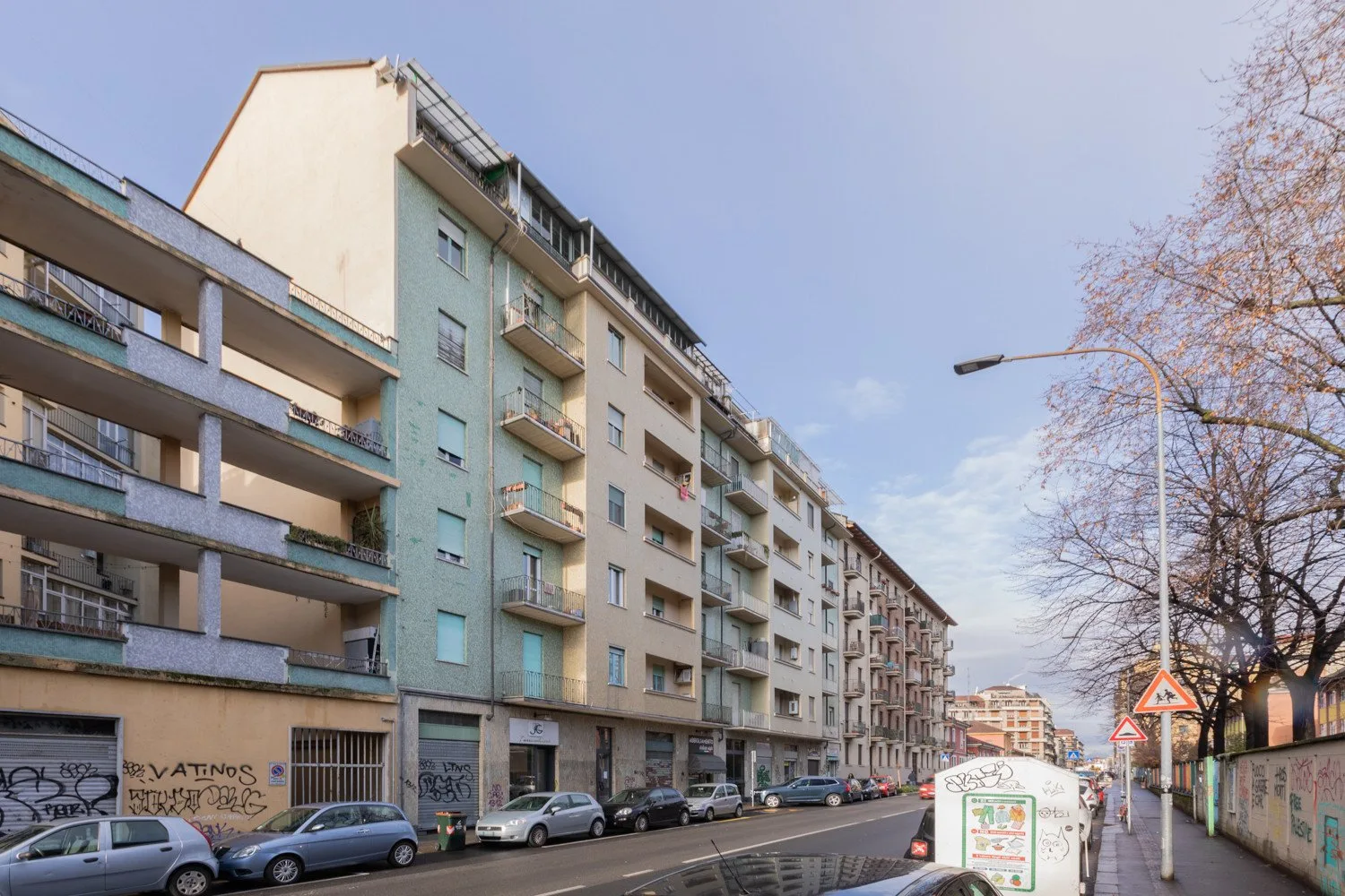 Una calle urbana con edificios de apartamentos, coches estacionados y una acera.