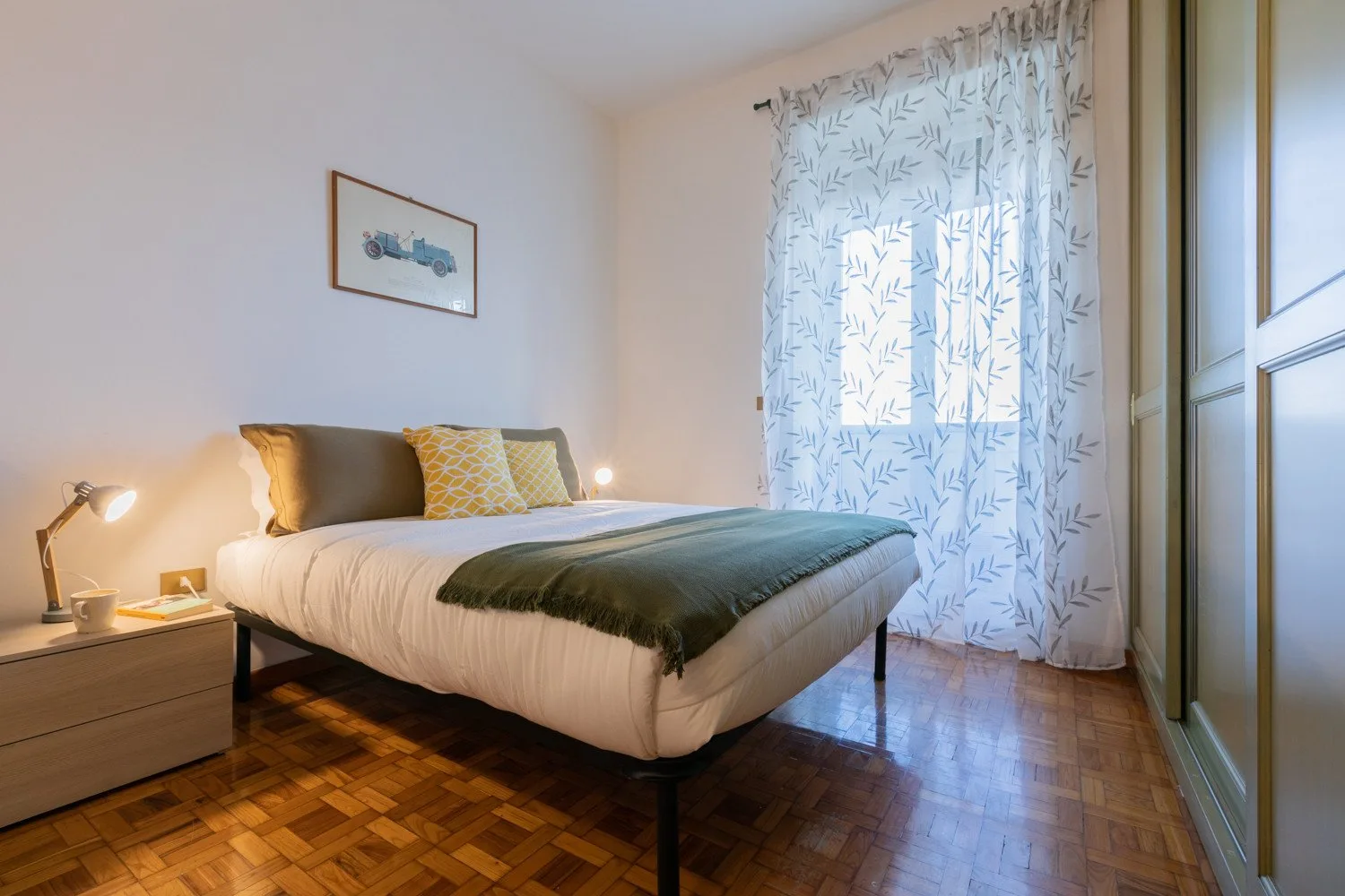 Un dormitorio con una cama, una mesita de noche y una ventana grande con cortinas.