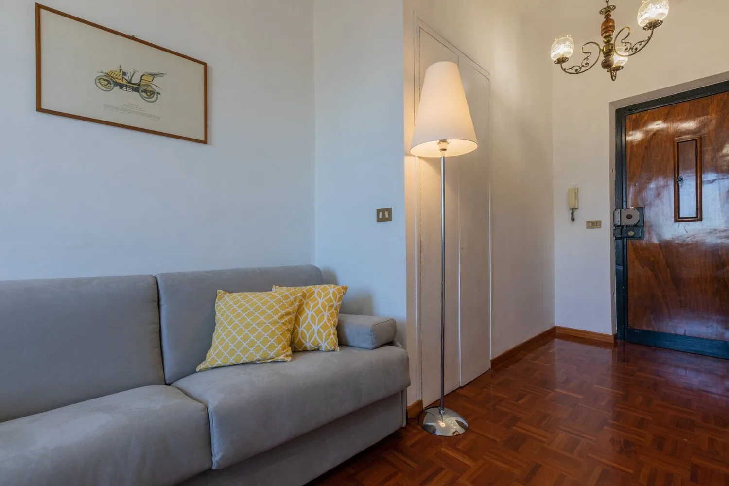 Una sala de estar con un sofá gris, cojines amarillos y una puerta de entrada de madera.