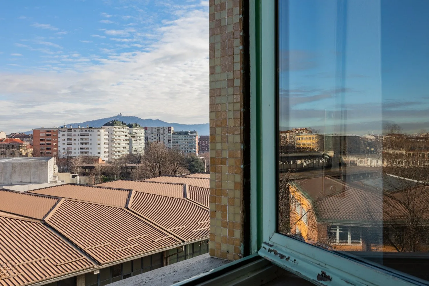 Una ventana da a edificios y tejados de la ciudad bajo un cielo parcialmente nublado.