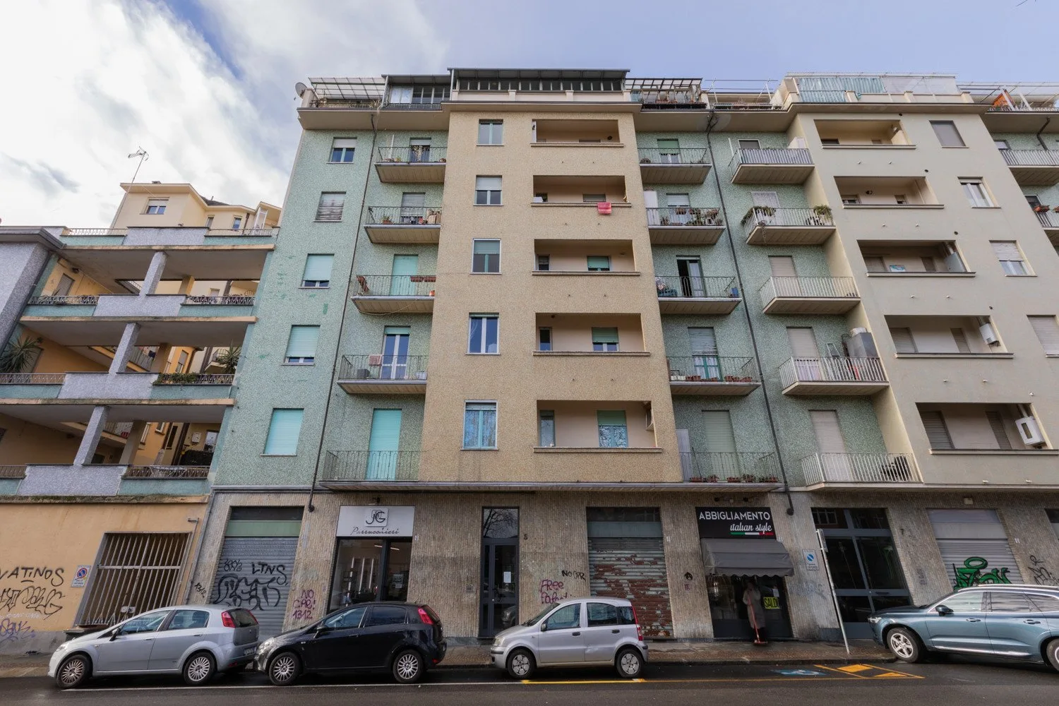 Vista a nivel de calle de un edificio de apartamentos con balcones y coches estacionados.