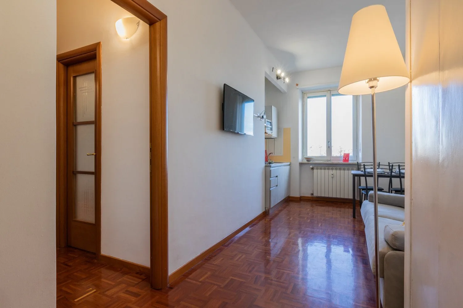 Una luminosa sala de estar y comedor con un televisor en la pared y una mesa junto a la ventana.