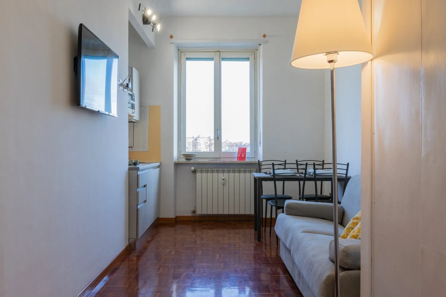 Una sala de estar pequeña con sofá, televisor y una mesa junto a la ventana.