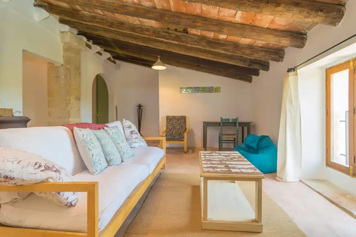 A bright living room with seating, a coffee table, and exposed wooden ceiling beams.