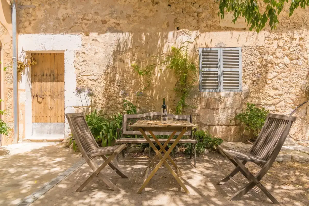 A shaded stone courtyard with a wooden table and outdoor seating.