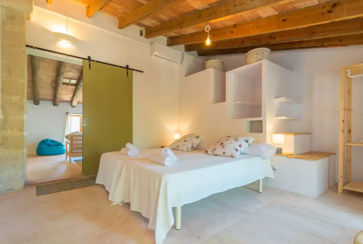 A bedroom with a bed, white linens, and exposed wooden ceiling beams.