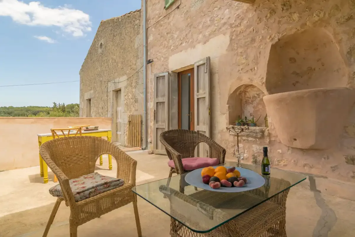 A stone terrace has wicker seating around a glass table with fruit.