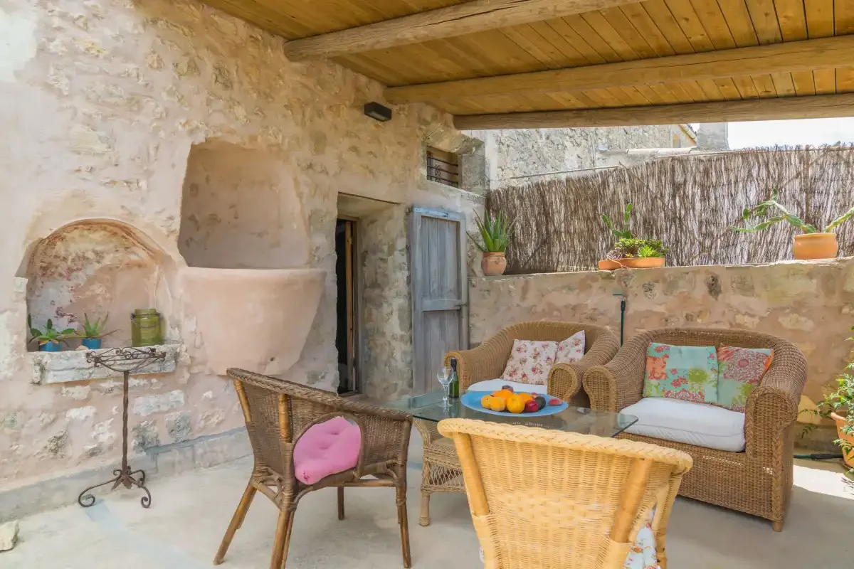 A covered stone patio with wicker seating and a low table.