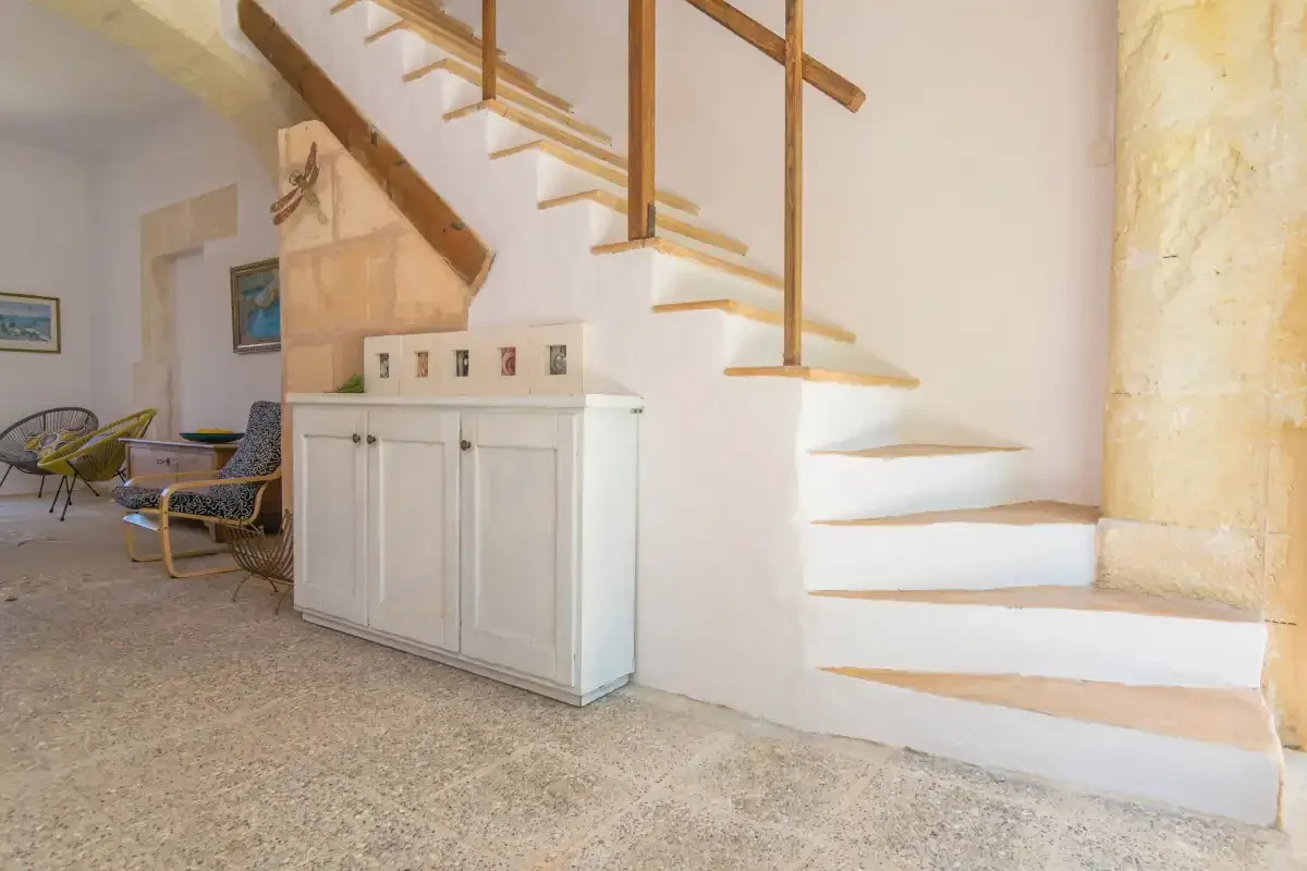 An interior staircase with wooden handrails rises beside a white cabinet.