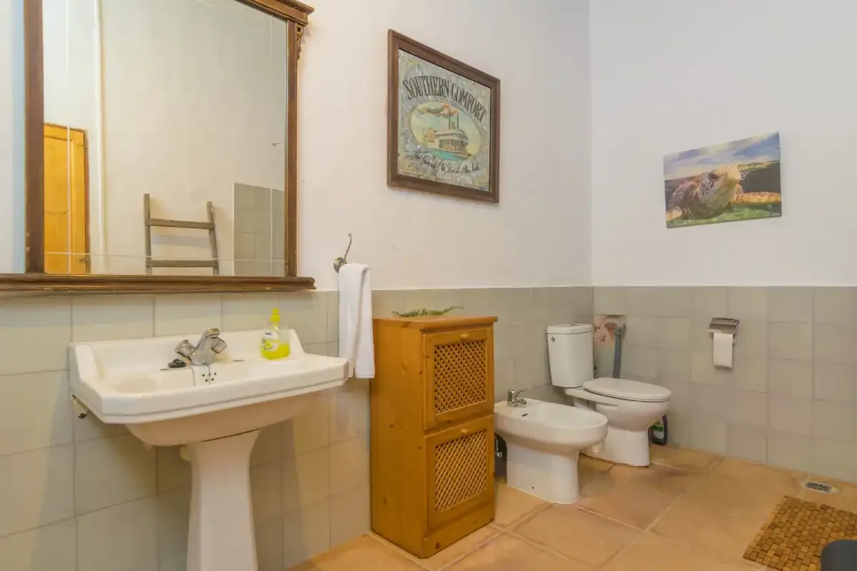 A bathroom with a sink, toilet, bidet, and wooden cabinet.