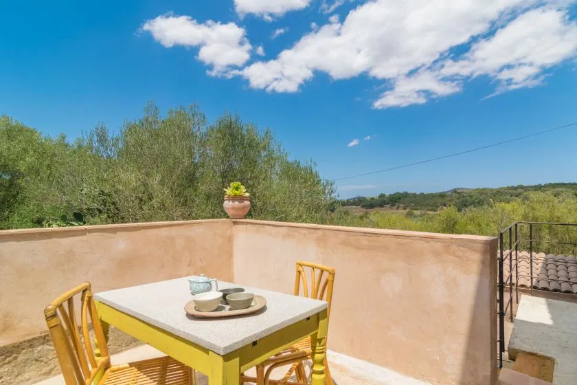 An outdoor terrace has a dining table set with dishes and overlooks green hills.