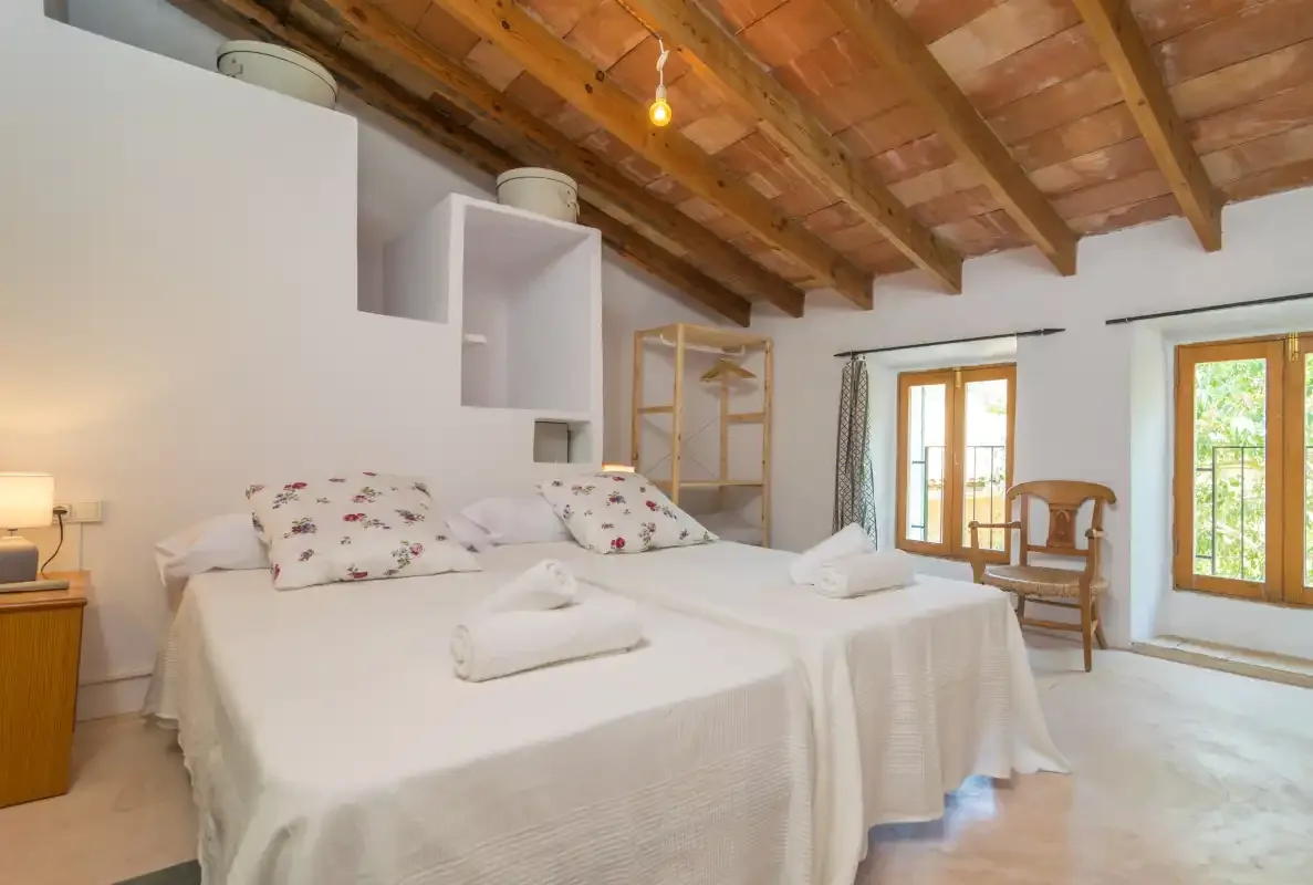 A bright bedroom with two beds beneath an exposed wooden ceiling.