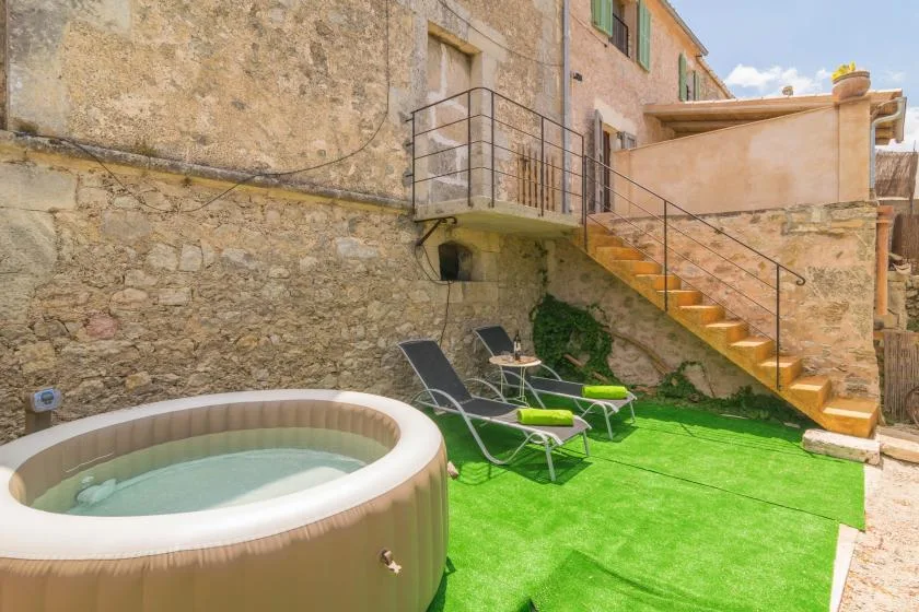 A small outdoor patio with a round hot tub, lounge seating, and stairs.