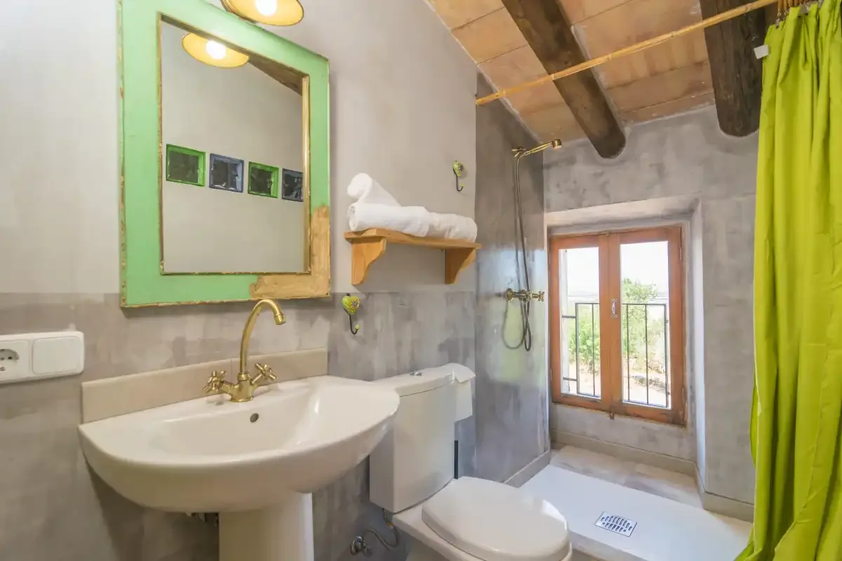 A bathroom with a sink, toilet, and shower beside a window.