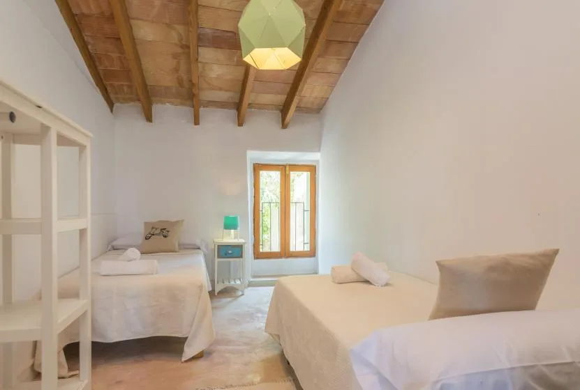 A bright bedroom with two beds and a window beneath a wooden ceiling.