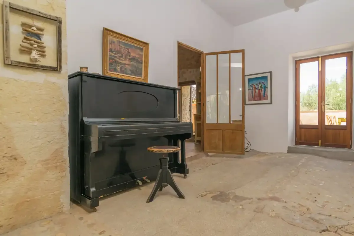 A black upright piano stands in a bright room with framed artwork and an open doorway.