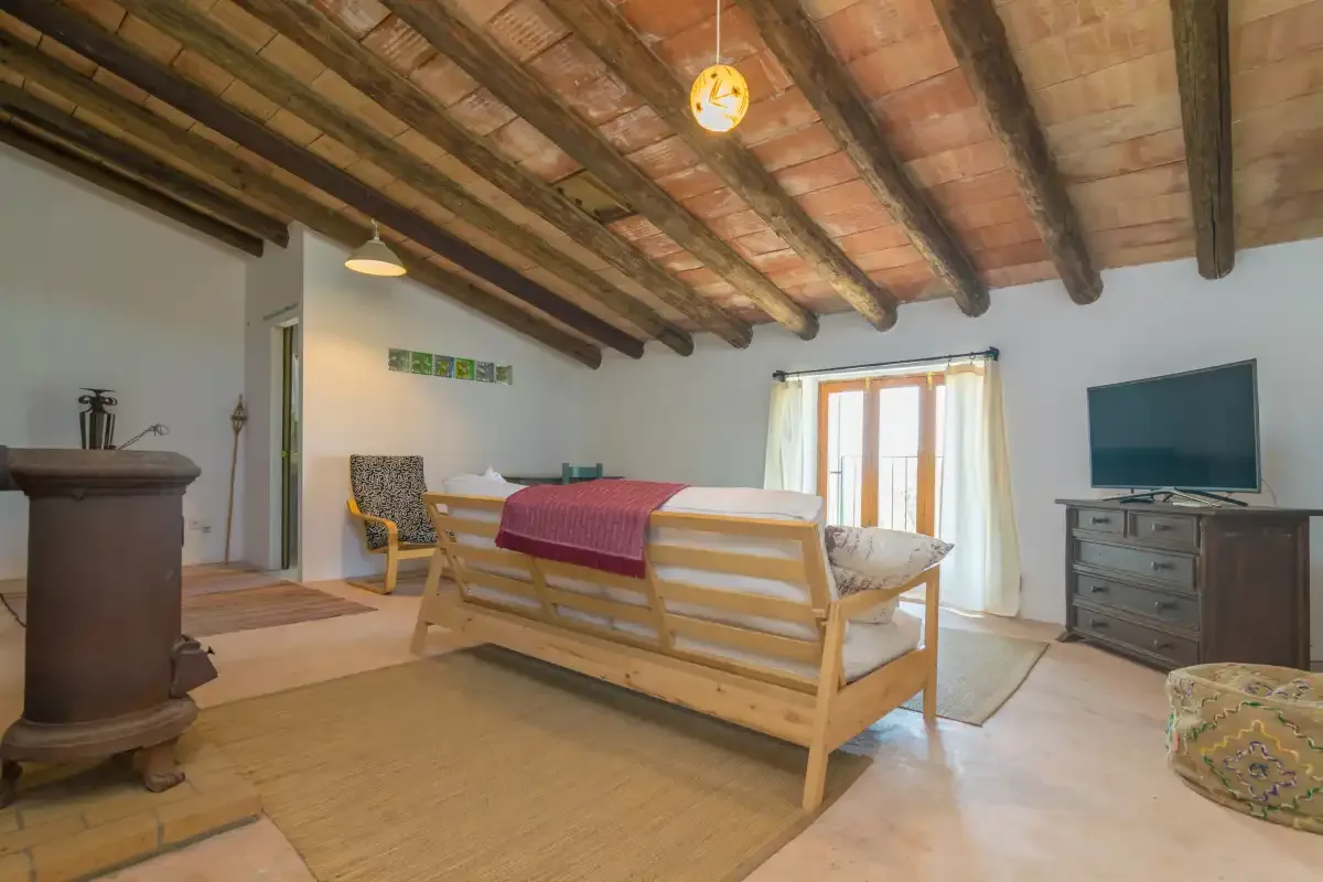 A living room with wooden seating, a television, and exposed ceiling beams.