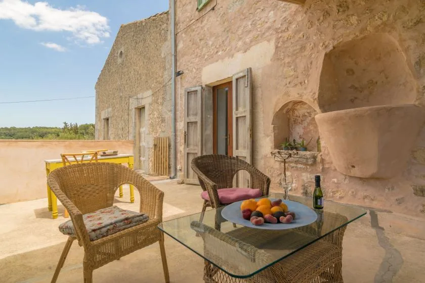 A stone terrace has wicker seating and a glass table with fruit.