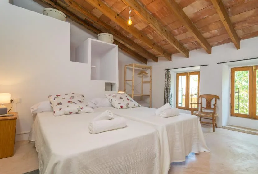 A bright bedroom with two beds beneath exposed wooden ceiling beams.