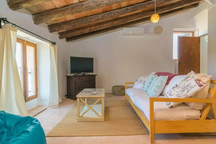 Living room with exposed wooden ceiling beams, seating, and a television.