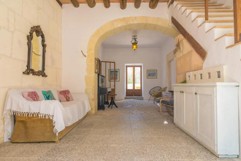 A bright stone interior with seating beneath an arch and a staircase.