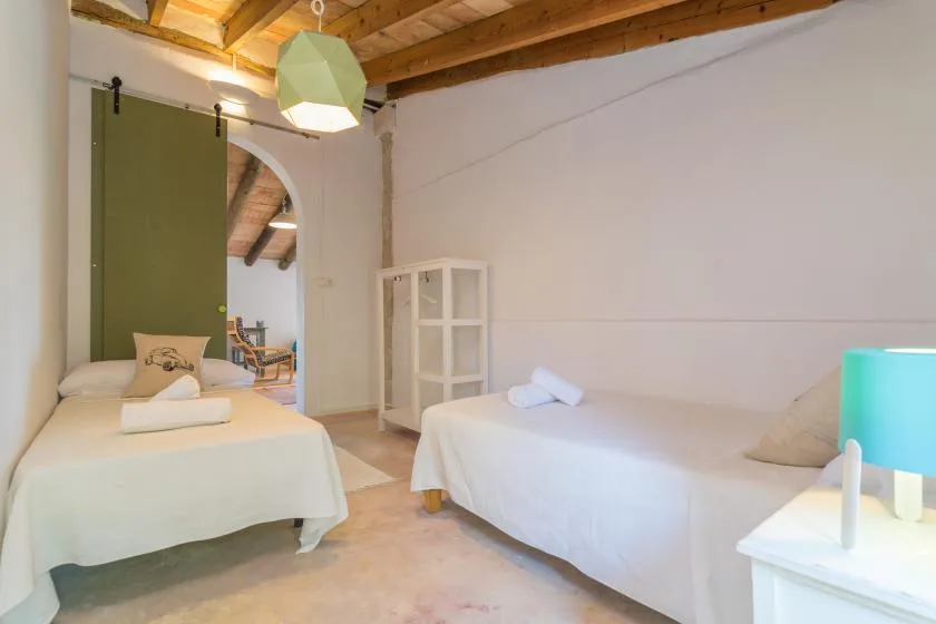 A bedroom with two beds, a white shelving unit, and exposed wooden ceiling beams.