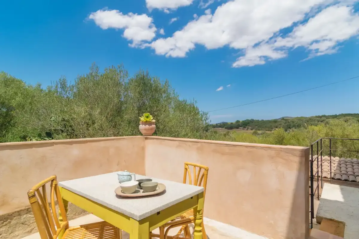 An outdoor terrace has a dining table and seating overlooking green hills.