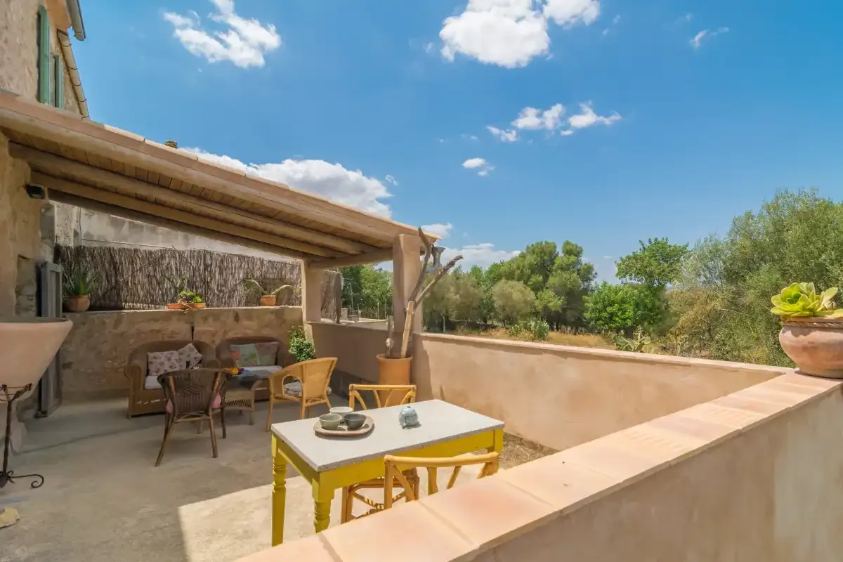 A sunny outdoor terrace with a dining table, seating, and views of greenery.