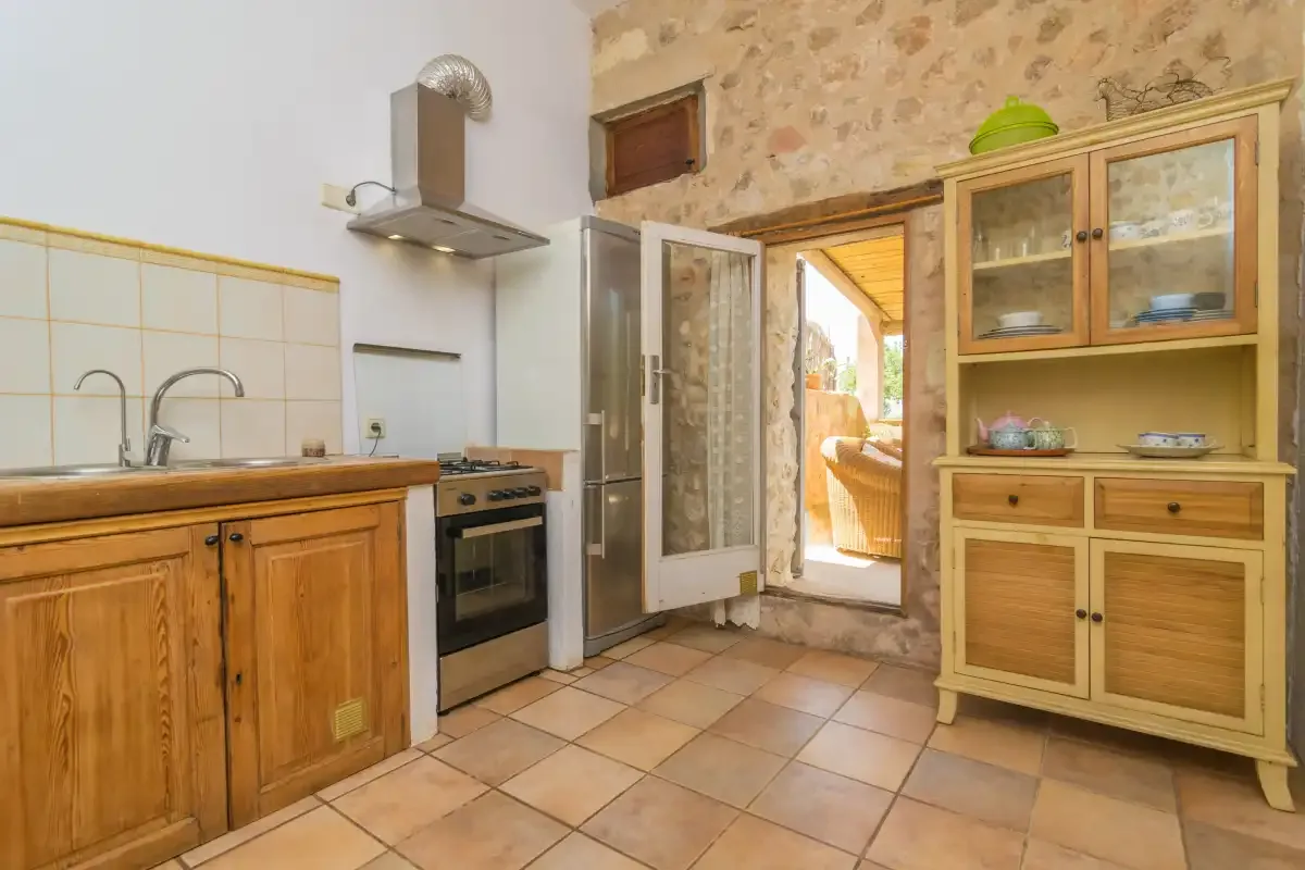 A rustic kitchen with wooden cabinets and an open doorway to a bright outdoor area.