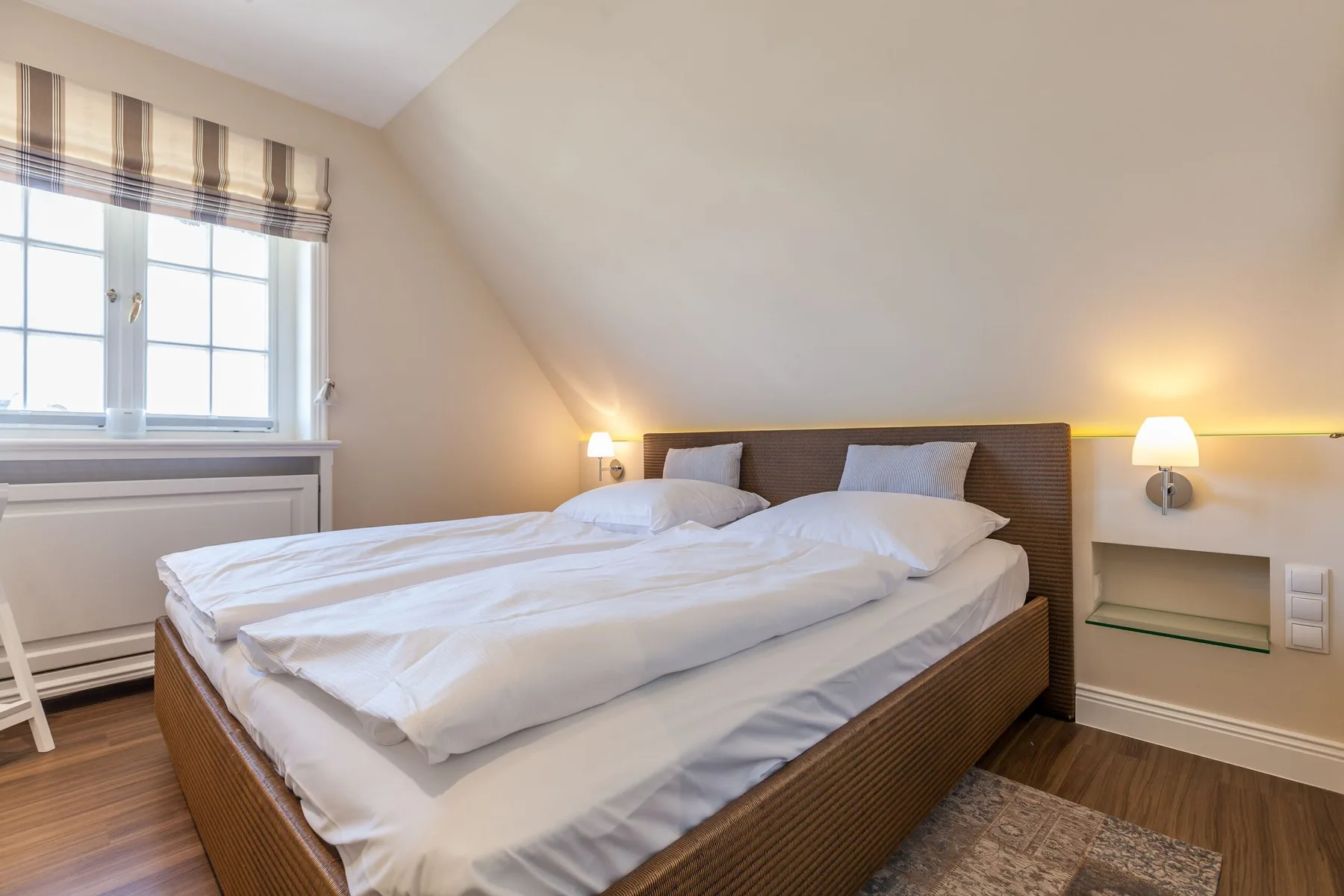 Un dormitorio con una cama bajo un techo inclinado y una ventana.