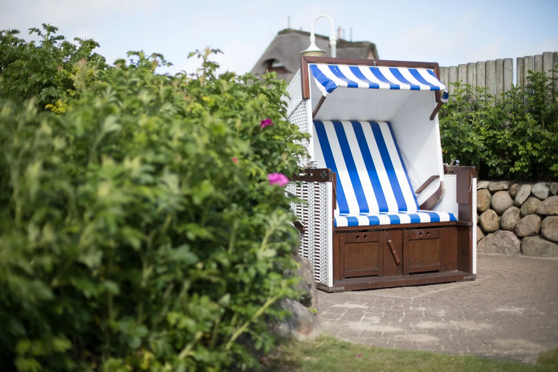 Una silla de playa a rayas está en un patio pavimentado junto a arbustos frondosos.