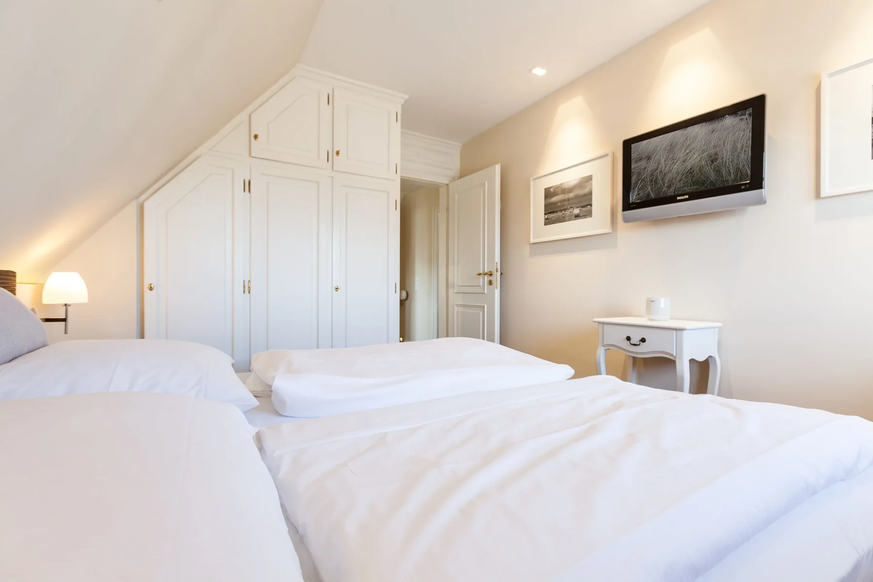 Un dormitorio luminoso con ropa de cama blanca, armarios empotrados y cuadros en la pared.
