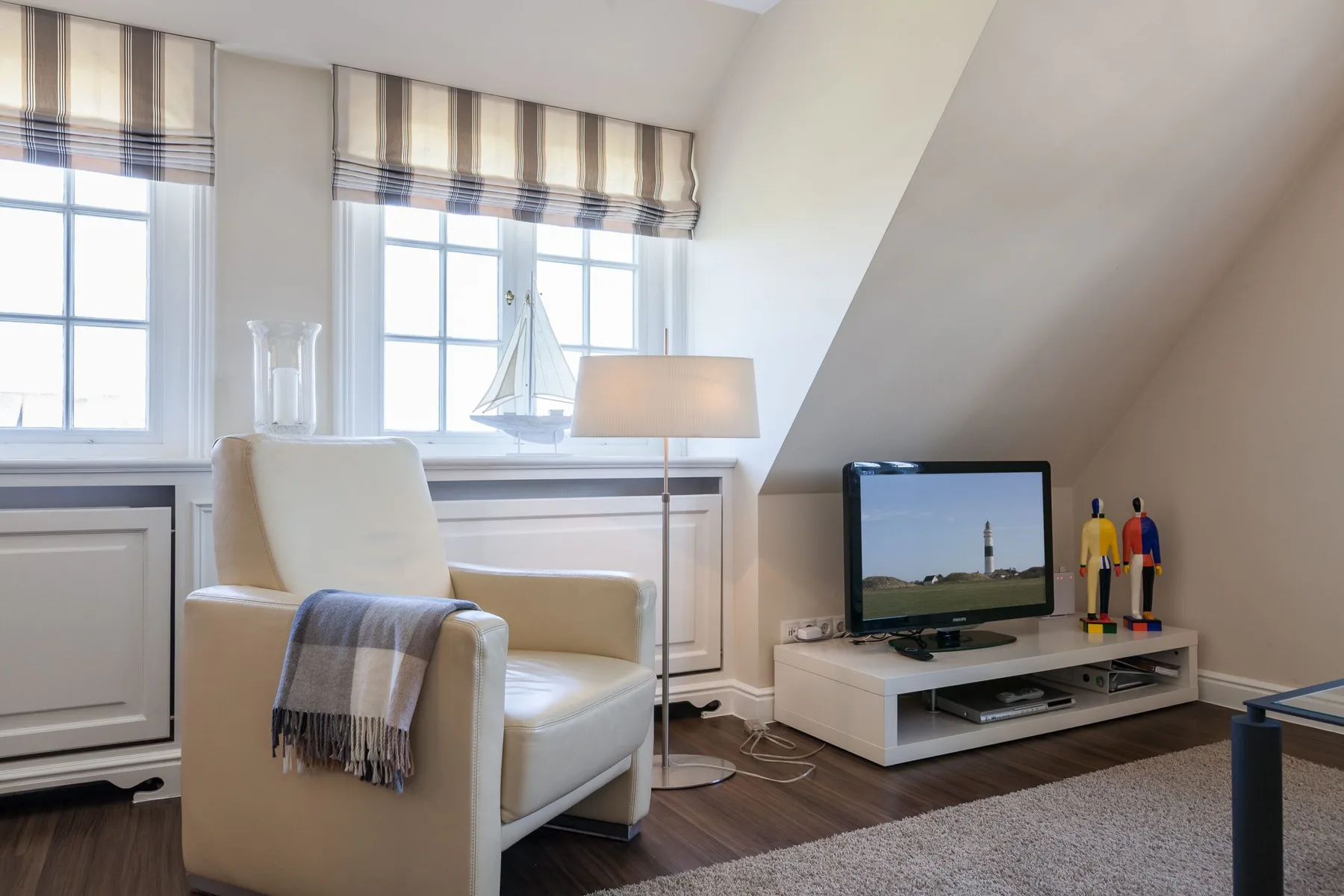 Una luminosa sala de estar abuhardillada con un sillón, televisor y techo inclinado.