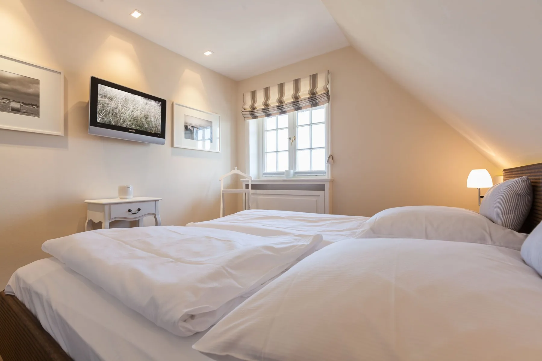 Un dormitorio luminoso con una cama grande, una ventana y cuadros en la pared.