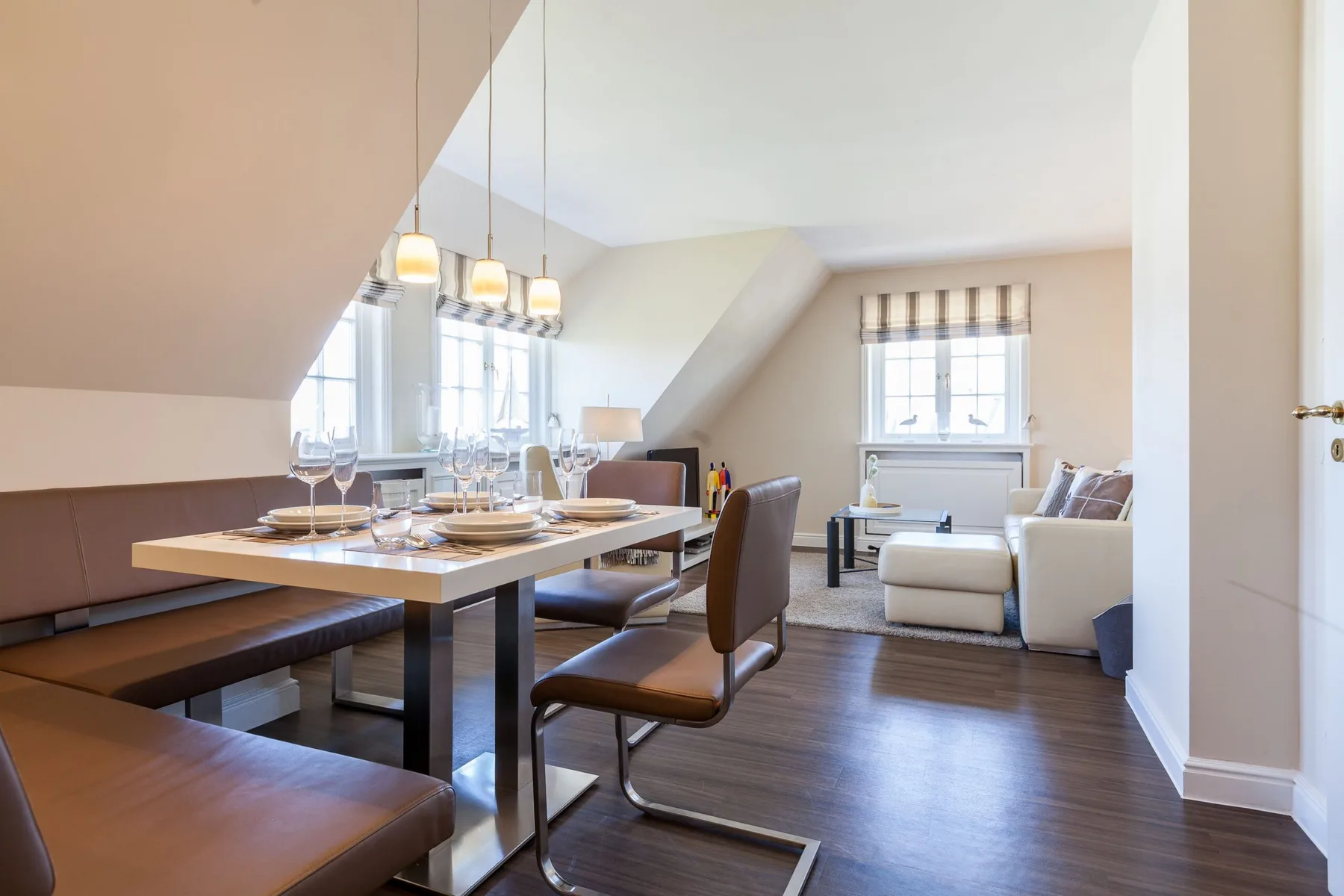 Zona de comedor y estar con la mesa puesta y asientos junto a las ventanas.