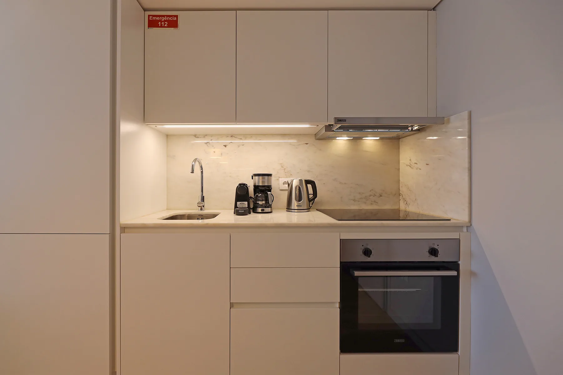 A compact kitchen with pale cabinets, a sink, and a built-in oven.