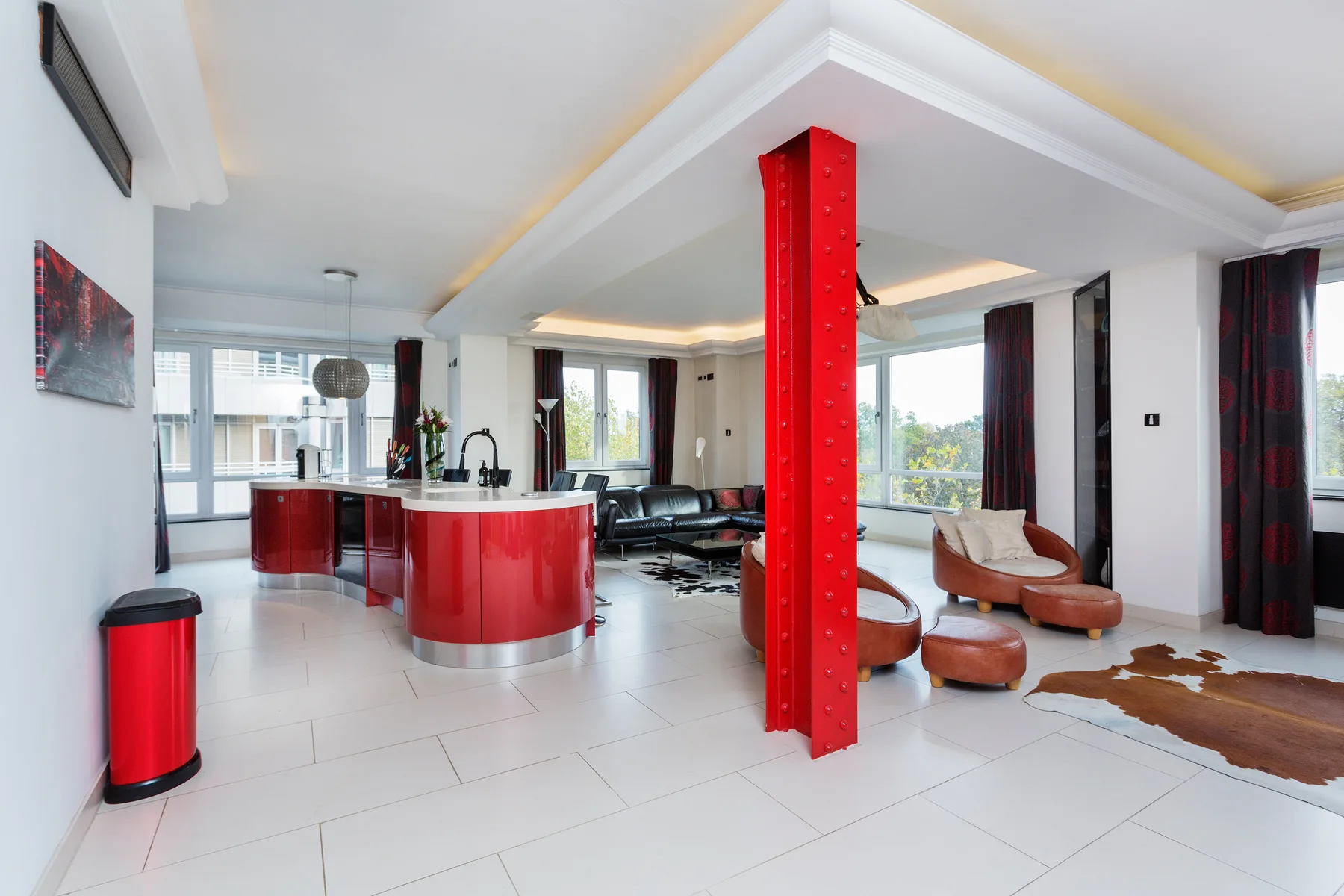 A bright open-plan living area with a red kitchen island and lounge seating.