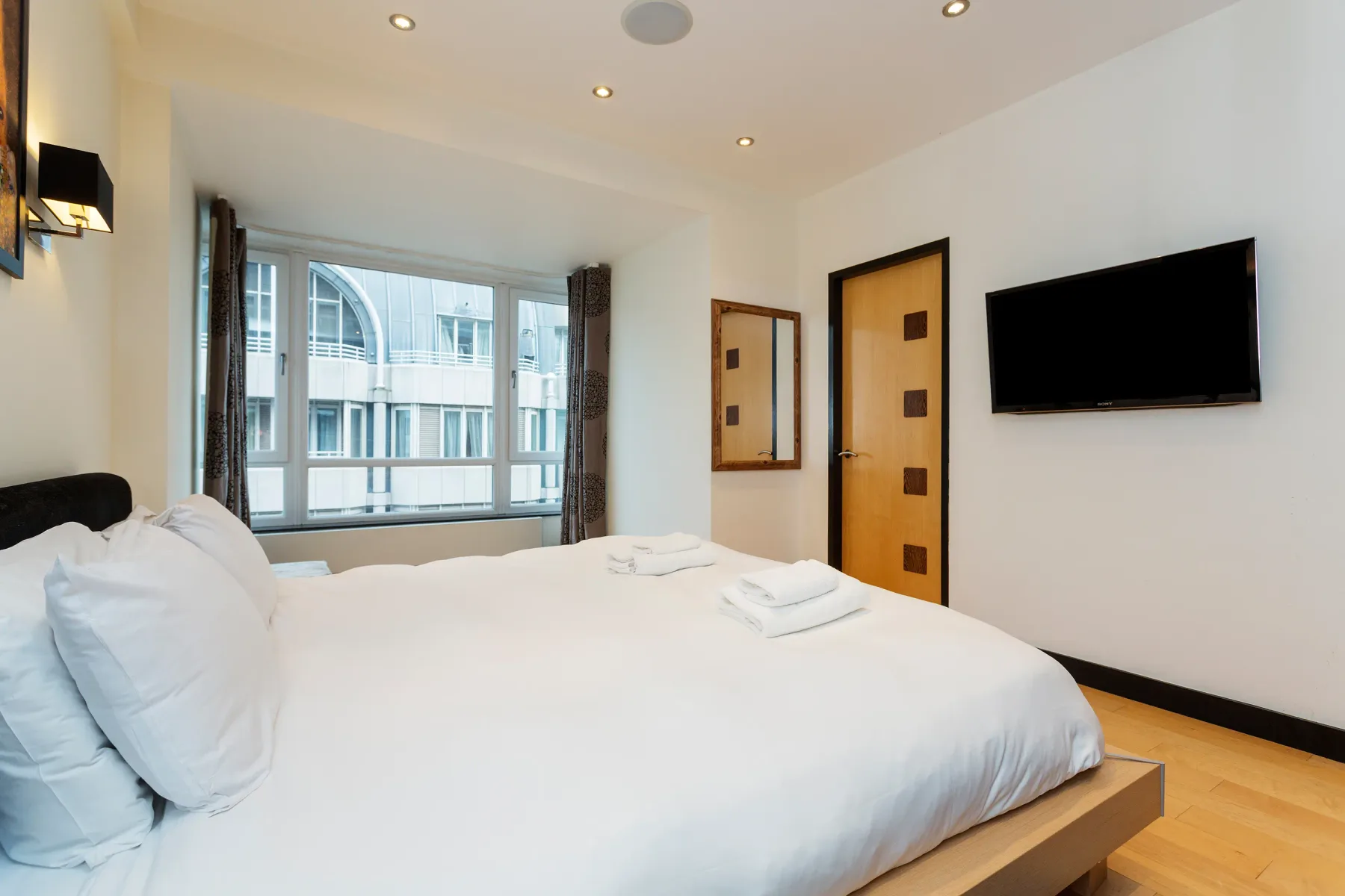 A bright bedroom with a neatly made bed and a wall-mounted television.
