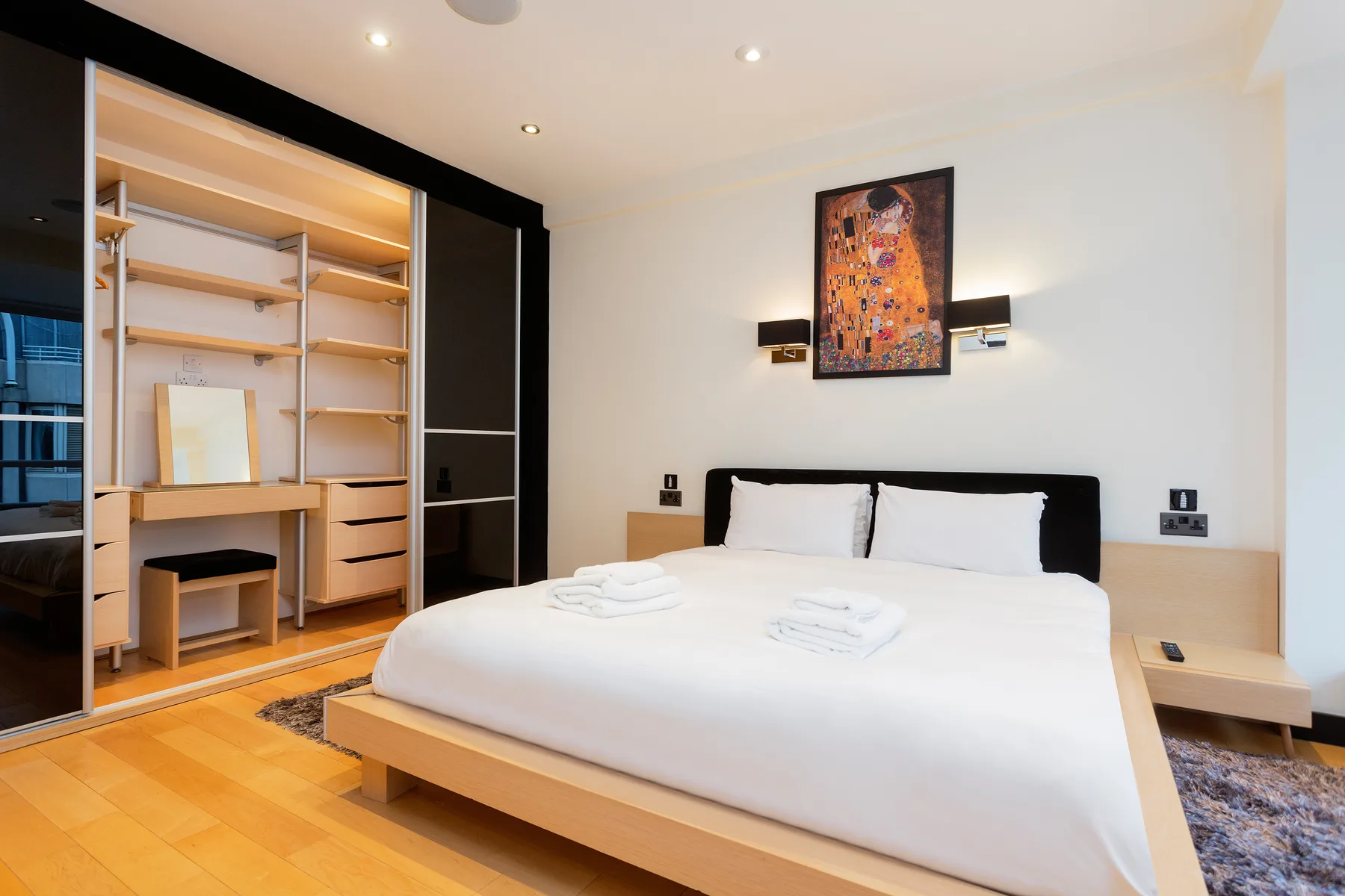 A bright bedroom with a neatly made bed and open shelving.