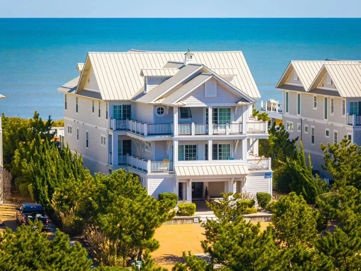 A large coastal house stands among trees beside the ocean.
