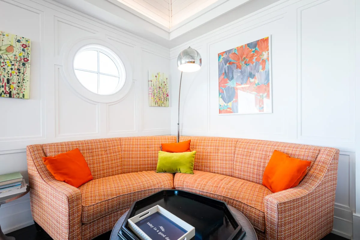 A bright living room with a curved orange-patterned sofa and colorful wall art.