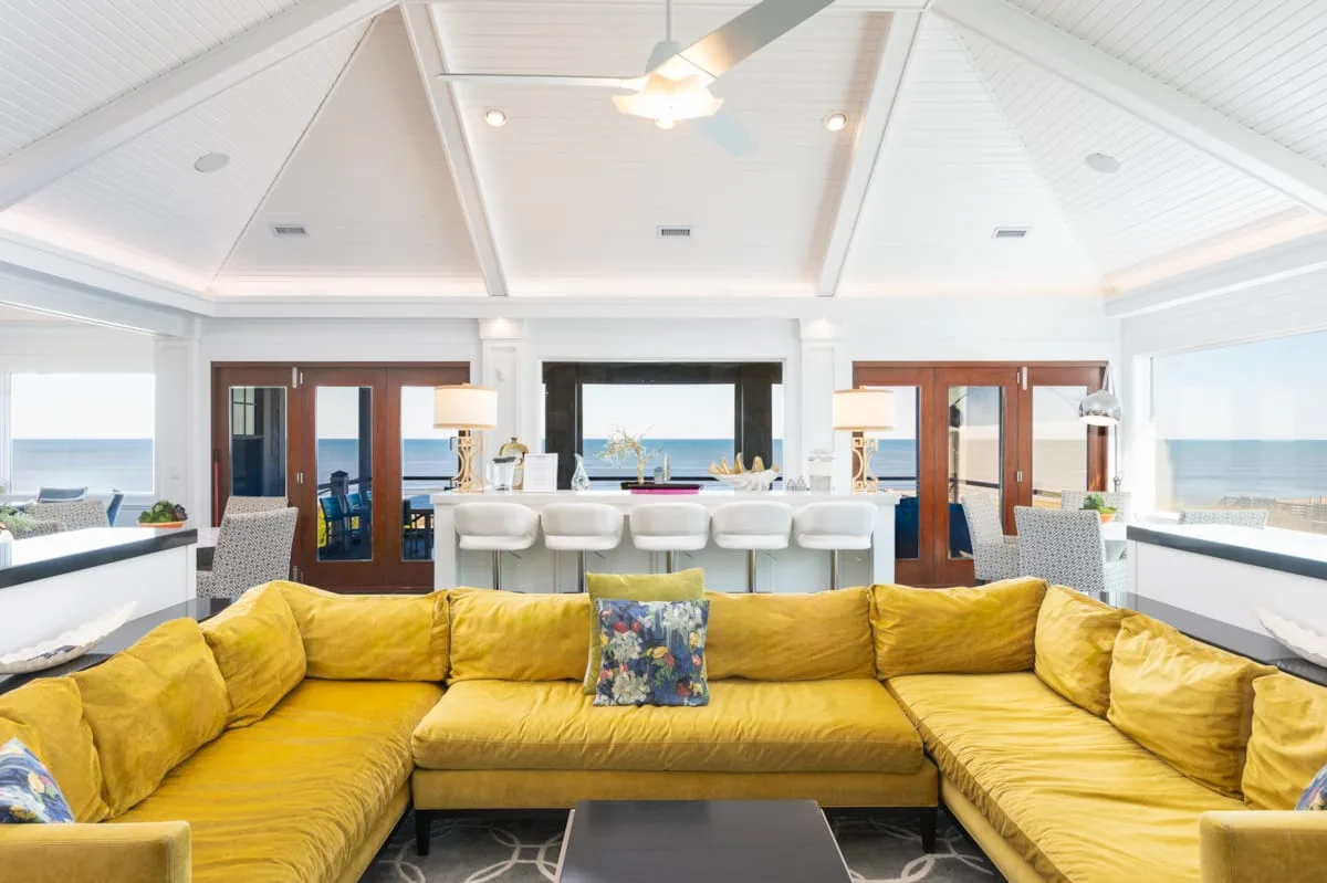 A bright living room with yellow sectional seating facing a kitchen island.