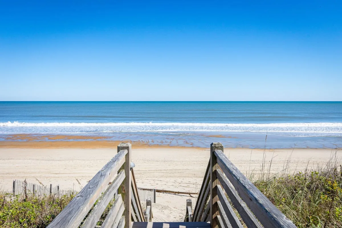 A wooden beach walkway leads across the sand toward the ocean.