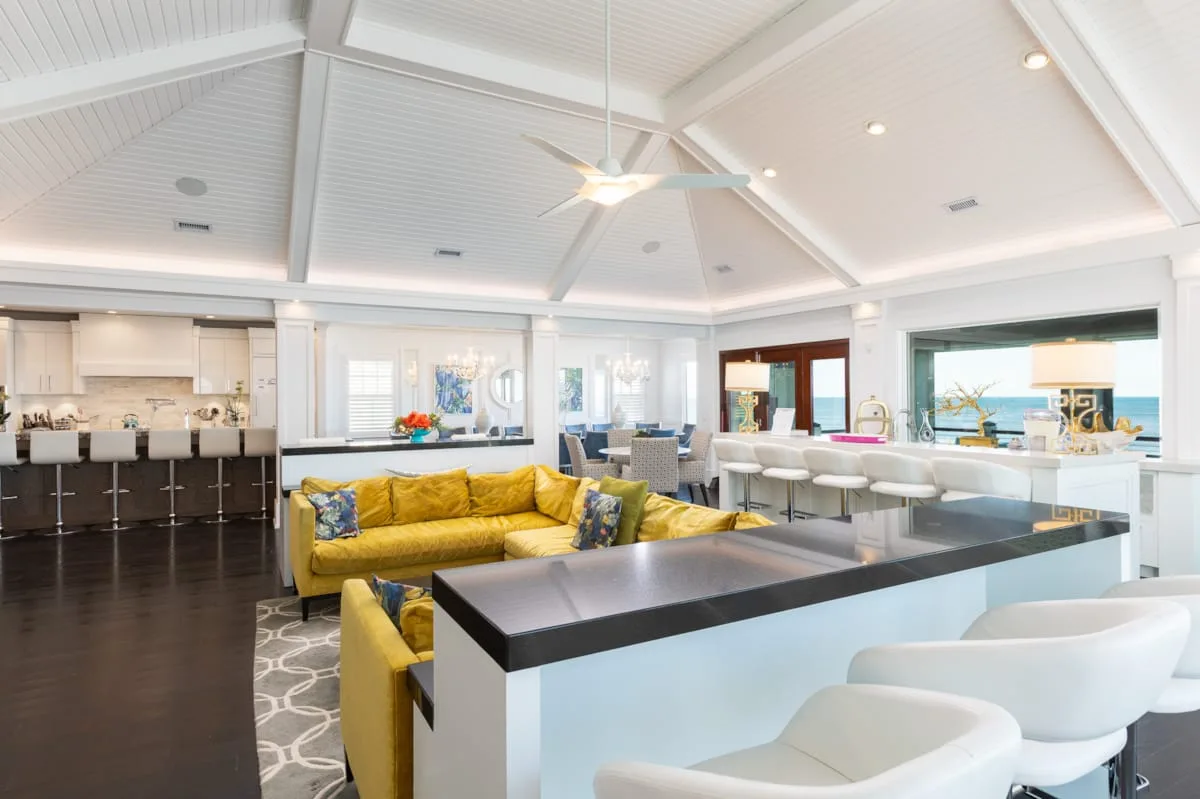 A bright open-plan kitchen and dining area features a yellow sofa and counter seating.